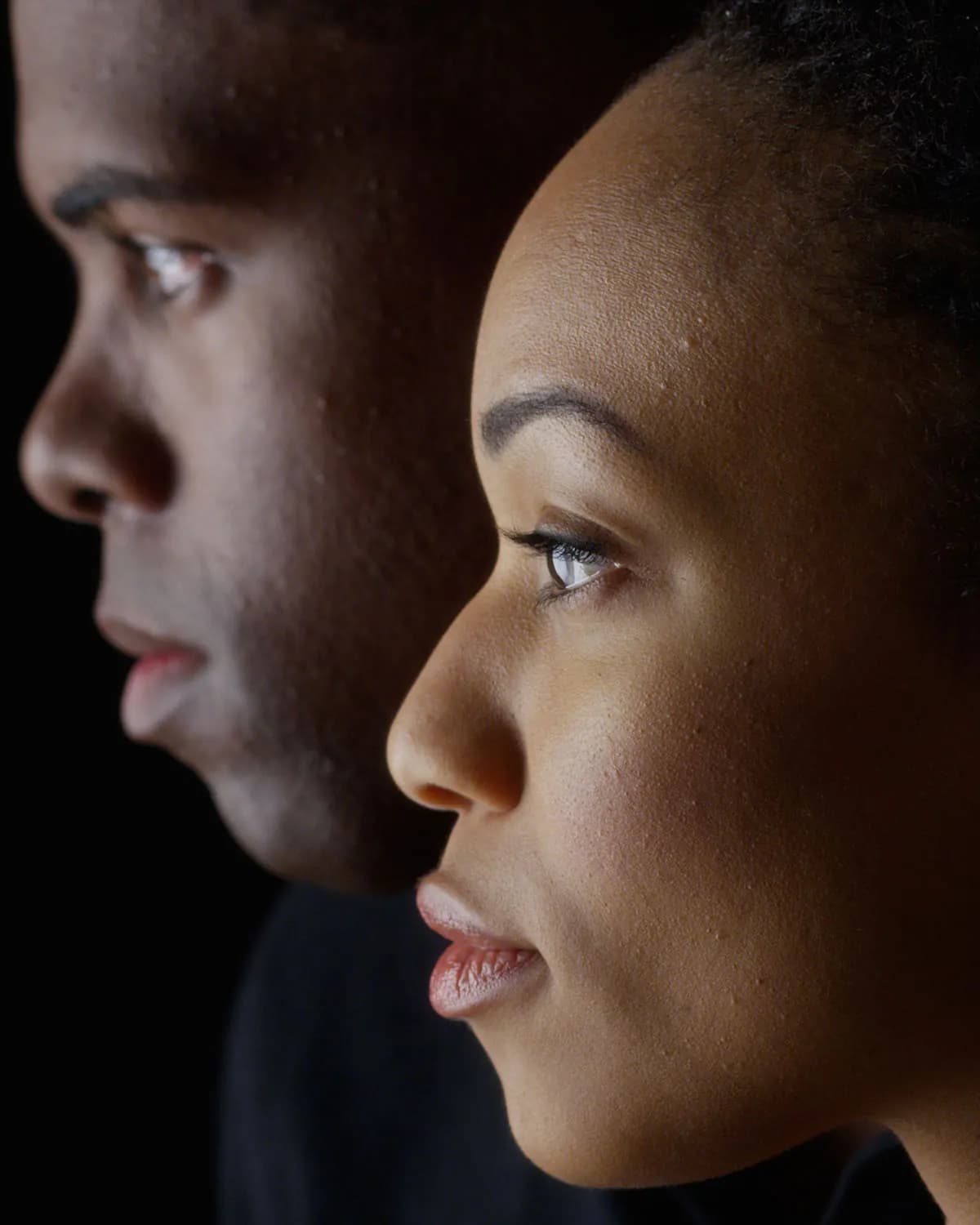 Dramatic side view of two young African American people on black background
